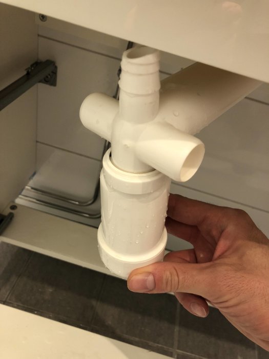 Hand som justerar avloppsledningar under handfat, med fokus på PVC-rörkopplingar.