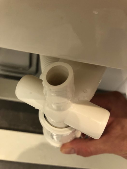 En hand som håller i en vit avloppsrörskoppling under ett handfat.
