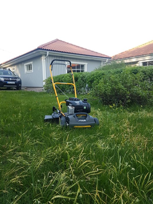 Ny gräsklippare från Stiga i högt gräs framför ett hus och en bil.