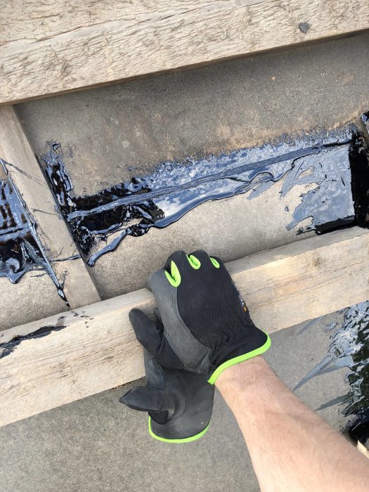 Reparation av tak med asfaltskitt, person i arbets handske applicerar kitt över trä och betongpannor.