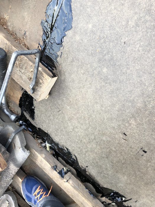 Reparation av tak med asfaltskitt kring ett större hål täckt av en träskiva, på ett tak med betongpannor.