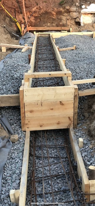 Armeringsjärn böjda för gjutning av betongfundament, med träform och grusunderlag.