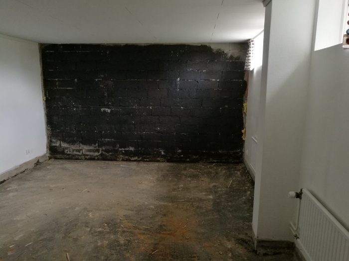 Rum med en vägg av svartmålade murblock och en rörande golv yta, i ett hus från 1969.
