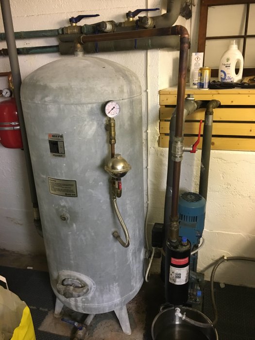 En hydrofor med ansluten motor och diverse VVS-rör och ventiler i ett pannrum.
