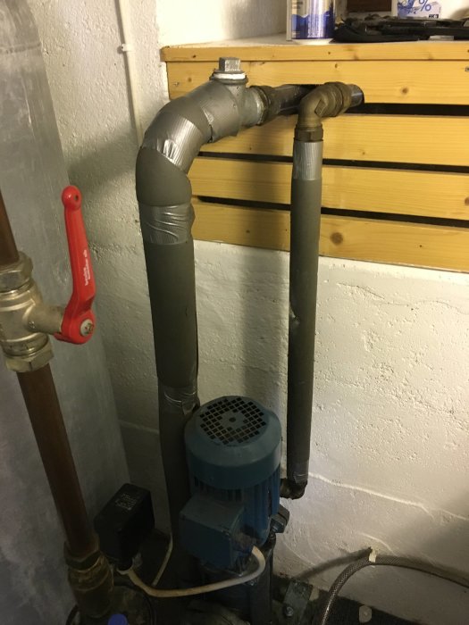 Ejektorpump och rörsystem i en källare med synliga ventiler och pump i förgrunden.