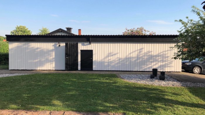 Ett litet fristående hus med ny obehandlad vit träsarg, svart tak och dörr, står inför målningsprojekt.