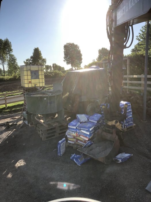 Byggplats med material och maskinell utrustning i morgonsol, material utlagt och klart.