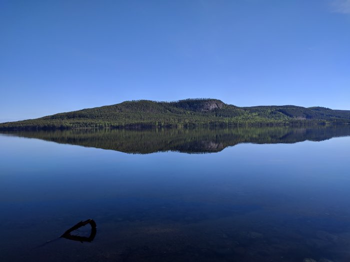 Tranquilt landskap med spegelblank sjö och skogklädda berg i Grötingen, perfekt för öringfiske.