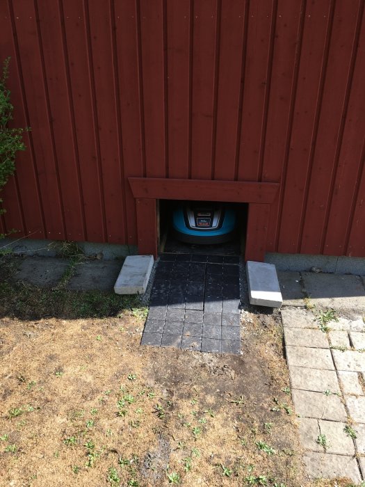 Rödmålat garage med öppen port där en robotgräsklippare står.