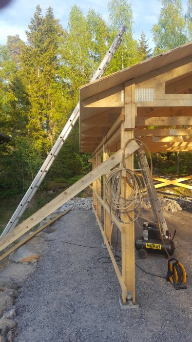 Semi-constructed wooden roof with rafter tails extending, scaffolding, and construction tools on the ground.