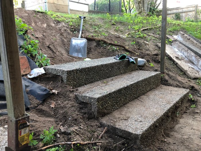 L-formade betongsteg i en trädgård under reparation med skottkärra och spade.