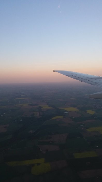Flygplansvinge med utsikt över landskap i solnedgång från luften.