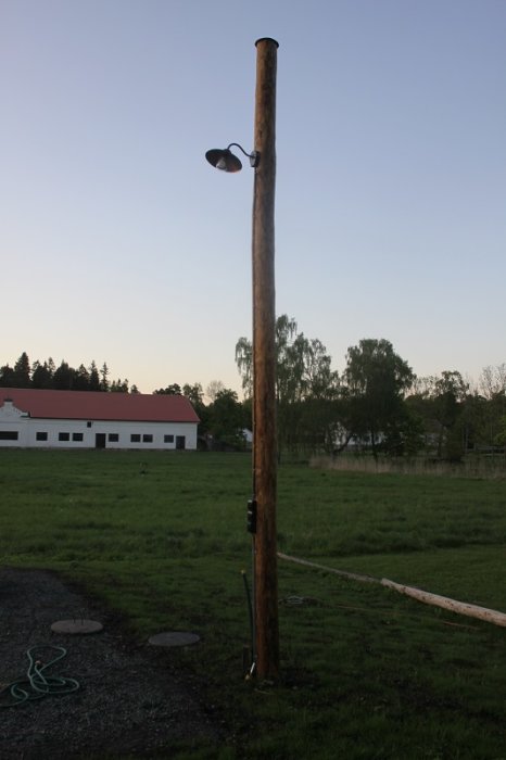 En nyligen färdigställd lyktstolpe i trä med en lampa och strömbrytare, placerad på en gräsmatta.