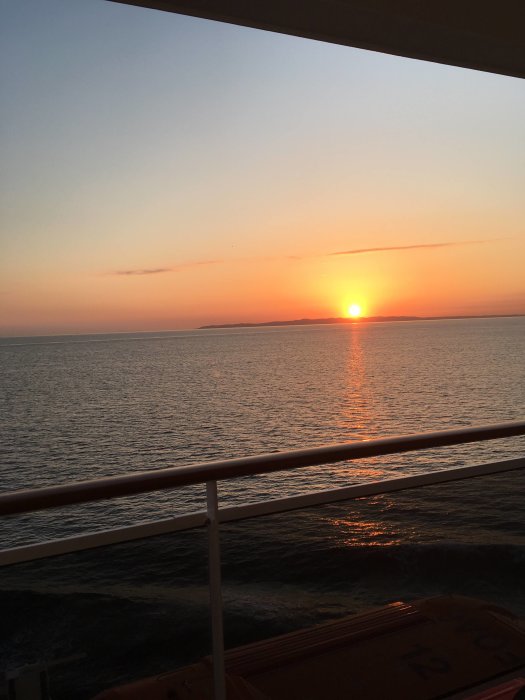Soluppgång över havet sedd från en balkong med räcke i förgrunden.