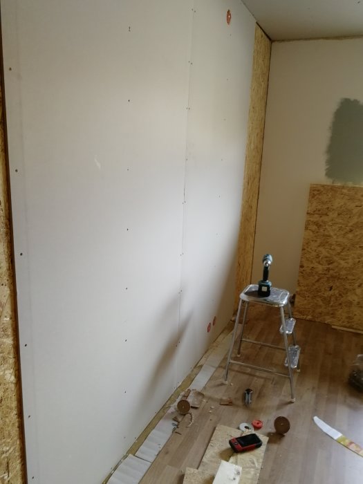 Renoveringsprojekt av sovrum med nya osb-gipsväggar och verktyg på golvet, i förberedelse för badrumsrenovering.