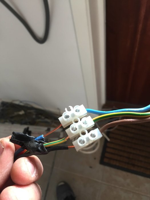 Person som håller i elektriska kablar och kopplingsklämmor under arbete med elinstallation.