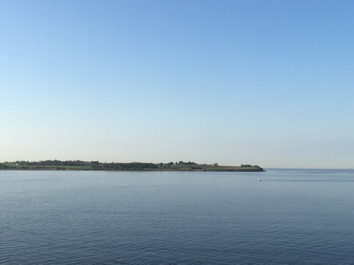 Kustlandskap med lugnt hav och en klarblå himmel.