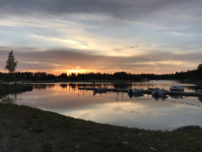 Solnedgång över en lugn sjö med båtar förtöjda vid bryggor och reflektioner i vattnet.