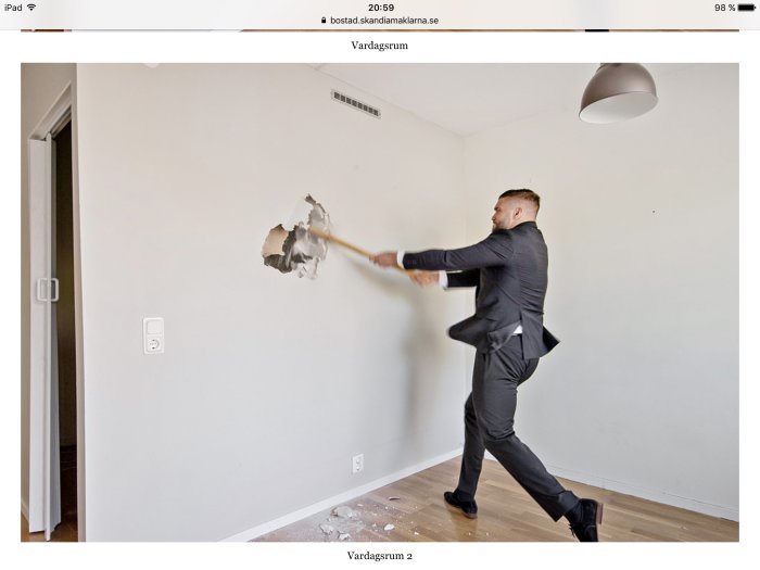 Man i kostym som slår sönder en vit vägg med ett verktyg under en renovering.