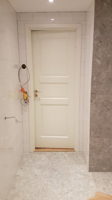 Vit dörr mot vit vägg med grå fogar, grå marmorkakelvägg och mosaikgolv.