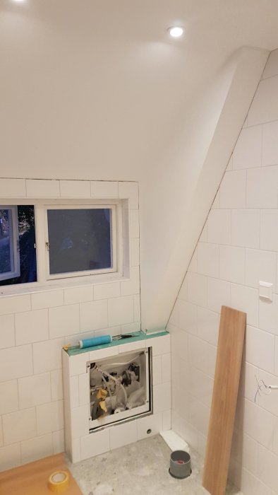 Renoverat rum med vit kaklad vägg, ett snedtak och ett fönster, redo för silikonfogning.