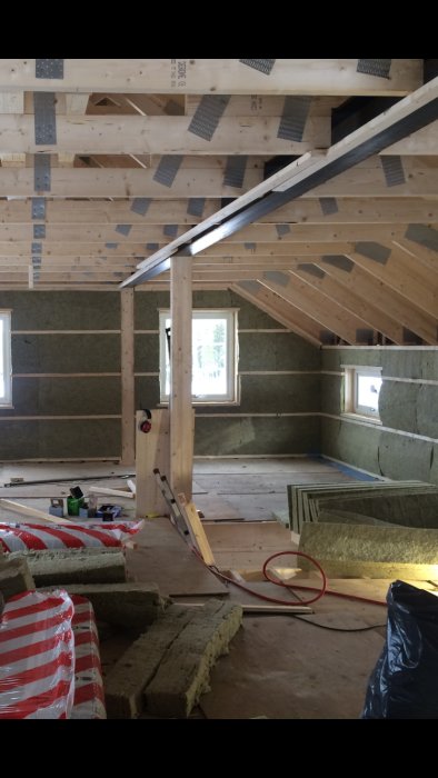 Inredning av vind med synliga takstolar, isoleringsmaterial och träreglar.