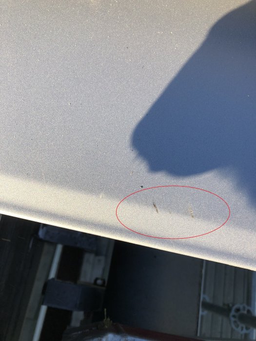 Närbild på en grå plåtyta med flera repor inom ett rödmarkerat område.