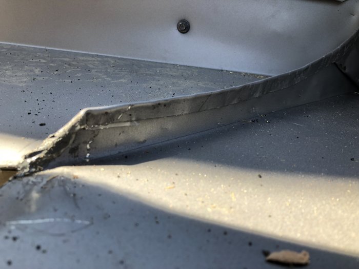 Närbild på en skadad och repad metallplåt, med synliga skador och en böjd kant.