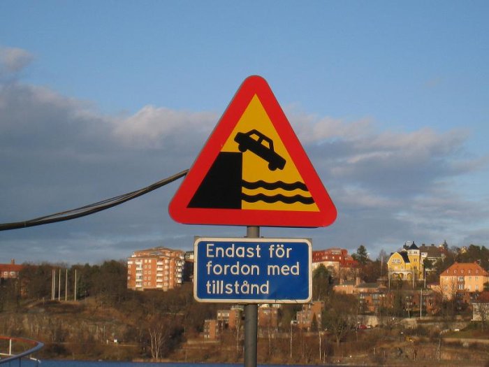 Trafikskylt som varnar för kajkant med texten "Endast för fordon med tillstånd" och Stockholm i bakgrunden.