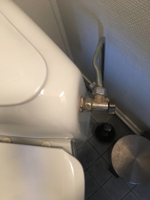Vit toalettcistern med stängt vattentillförselventil och synlig vägghängd vattenledning.