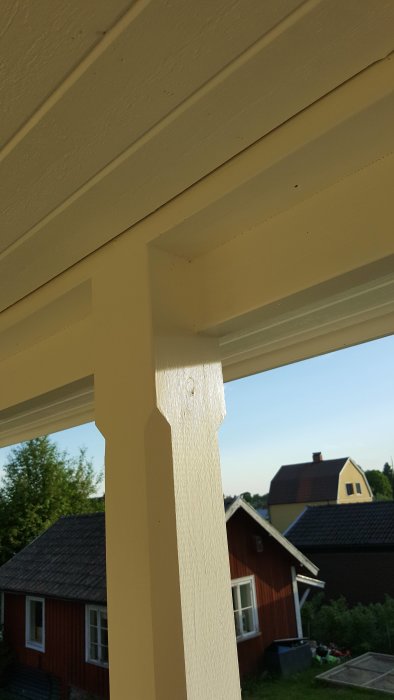 Urjackat trästolpe för balkskor på en veranda, med hus och träd i bakgrunden.