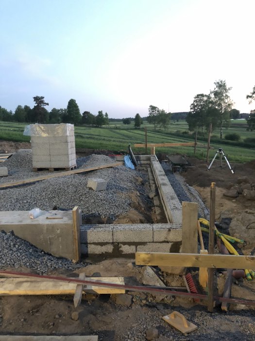 Grund av hus under konstruktion med betongblock och grusbädd i skymningen.