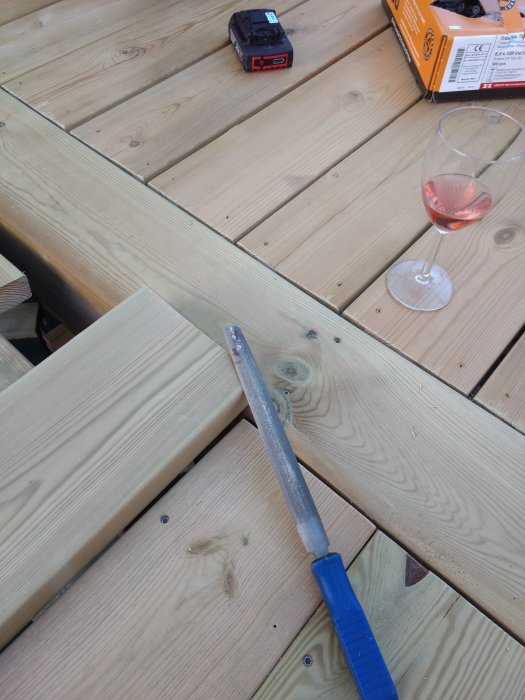 Trallbrädor på ett trädäck med en fil och skruvdragare, och ett glas rosévin till höger.