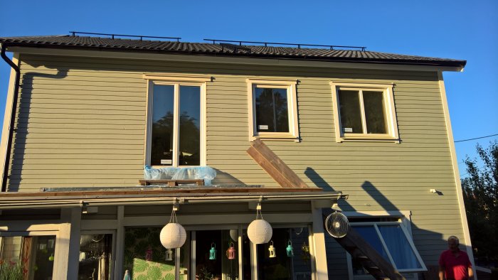 Nyinstallerad dörr på andra våningen av ett hus med träfasad, med montageplattform och byggmaterial synligt.