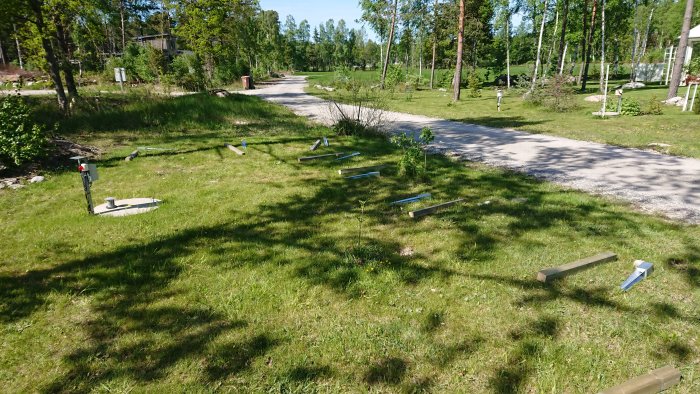 Staketbyggnadsprojekt, verktyg och material utspridda på gräs, förberedelse för jordankare och stolpar.