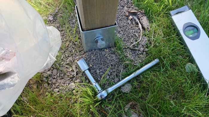 Jordankare och en byggdetalj monterad i marken vid staketstolpe, med fransk skruv och vattenpass.