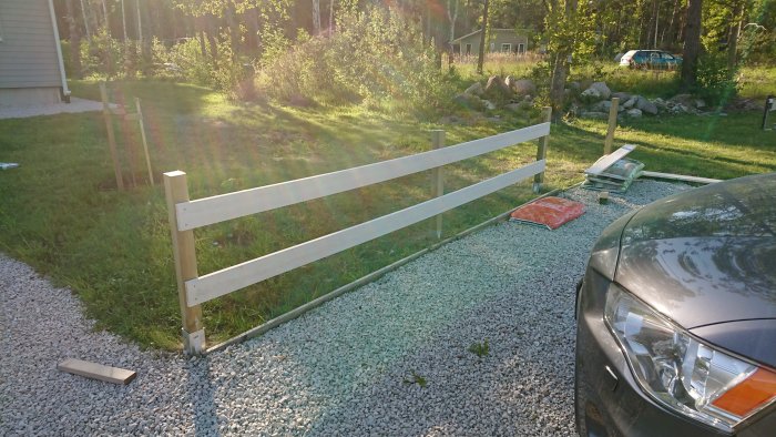 Nybyggt staket med tryckta stolpar och vitgrundade slanor i en trädgård med byggmaterial synligt.