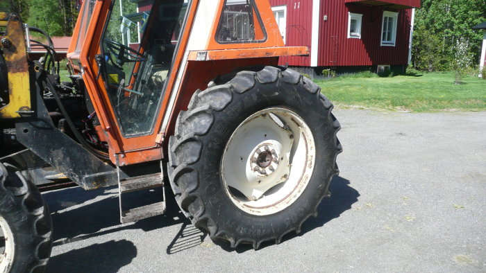 Närbild av ett kraftigt mönstrat jordbrukstraktordäck med röd traktor och röd stuga i bakgrunden.