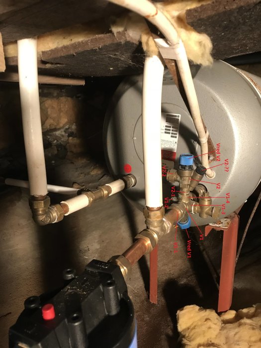 VVS-installation med etiketterade ventiler och rör kopplade till en varmvattenberedare under takbjälkar.