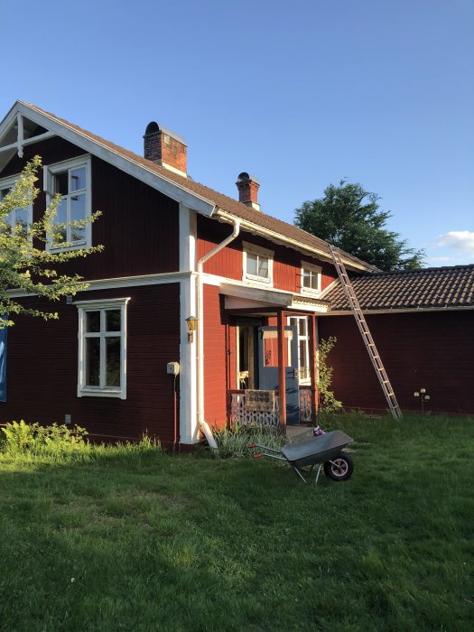 Traditionellt rött 1,5-plans trähus på landet med vitrapp och skorstenar, tidigt 1900-tals konstruktion.