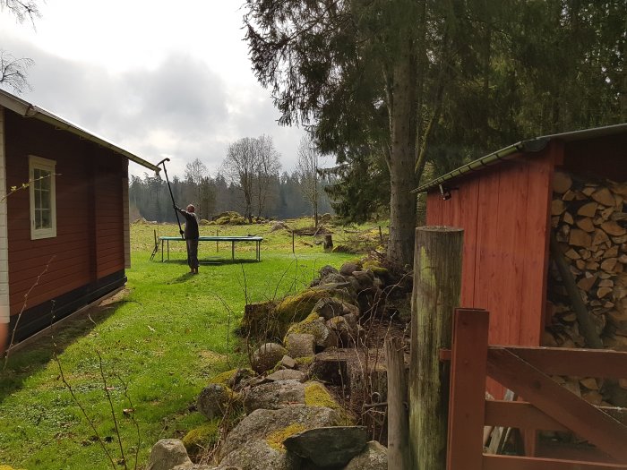 Hängränna fäst med krokar på röd träbyggnad till höger med staplad ved i förgrunden.