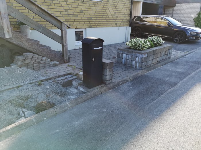 Delvis demonterad stenmur vid trottoar med brevlåda och uppbyggd stenplantering.