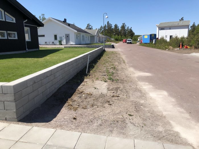 Stödmur vid hus med en smal jordremsa fylld med ogräs framför en gångväg.