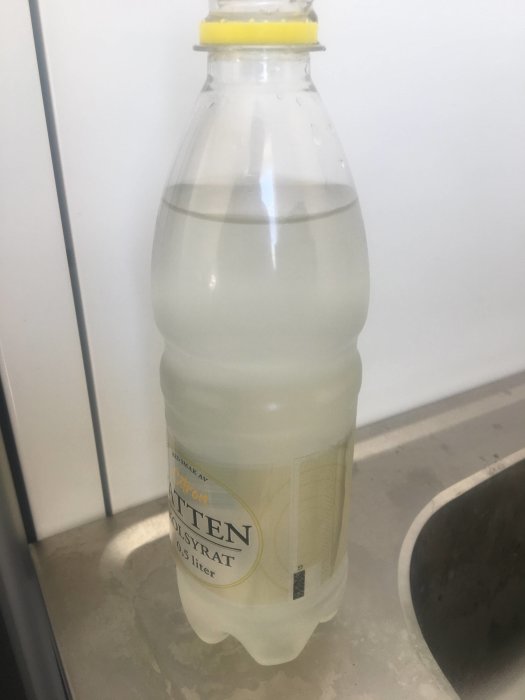 Plastflaska med grumligt vatten bredvid en diskho, indikerar problem med vattenkvaliteten i ett nybyggt hus.