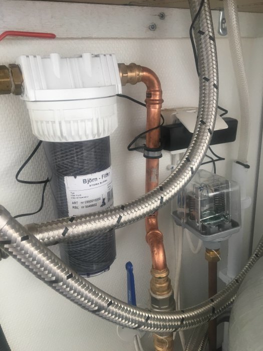 Vattenfilterinstallation med kopparledningar och sladdar i ett tekniskt utrymme.