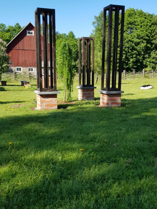 Trädgård med nyplanterat lärkträd och pelare med träkonst framför en röd lada.