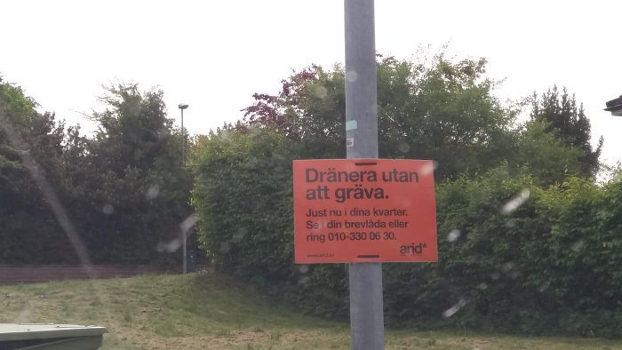 Skylt om dränering utan grävning från Arid fäst på stolpe med grönska i bakgrunden.