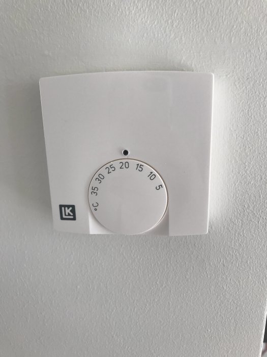 Vit termostat på vägg med graderingar från 5 till 35 grader och LK-logotyp.