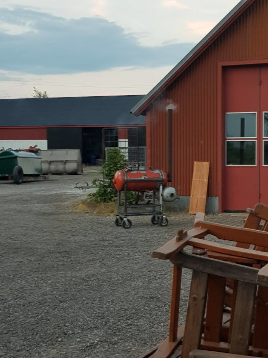 Utomhusbild på en röd byggnad med en grå cistern och en grill i förgrunden.