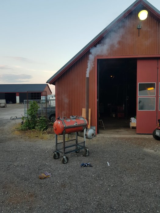 Röd ladugård med öppna dörrar, kompressor utomhus och verktyg på marken.